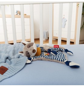 Doudou plat raton laveur bleu signé Sigikid dans le lit de bébé